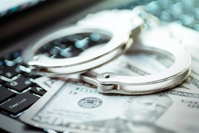 Spread of cash and a pair of handcuffs sitting on a computer keyboard depicting cybercrime, identity theft, fraud