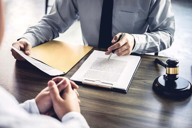 Mediator reviews case records as he sits at a desk with a gavel next to him on the desk while another businessman sits across from him with his hands clasped as he listens