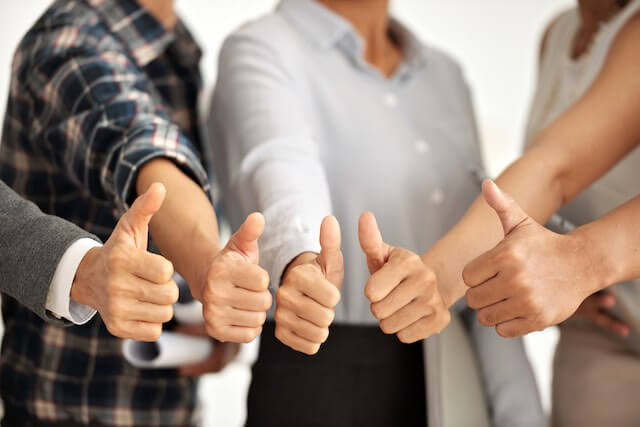 Close up of the hands of a group of four employees giving a thumbs up sign depicting high morale, team building, and happy employees