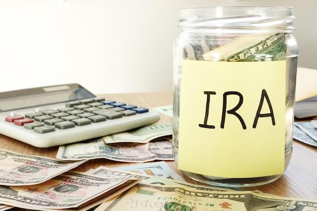 Jar sitting on a desk labeled 'IRA' next to a calculator and cash depicting retirement and financial planning