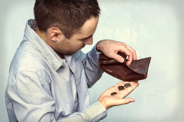 Man holding open his wallet to find no money and only a few coins falling into his hand as he appears worried that he has no money