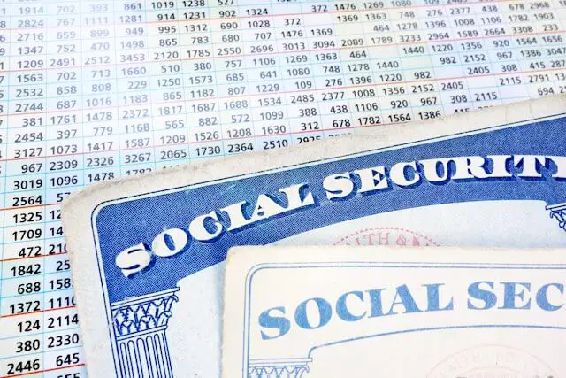 Two Social Security cards pictured on top of a spreadsheet of numbers