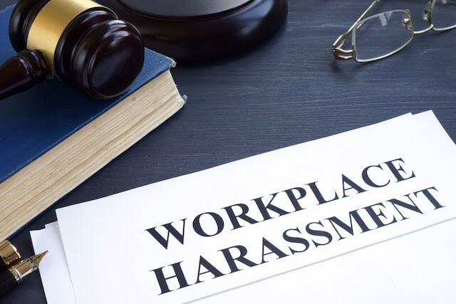 Document on a desk labeled 'workplace harassment' next to a law book and a judge's gavel