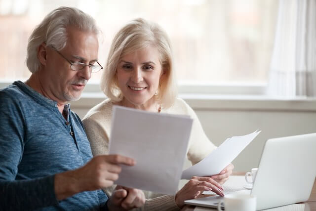Senior aged couple appearing happy as they sit together at a desk looking over paperwork