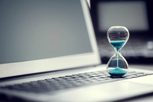 Hourglass with sand pouring down through it sitting on the keyboard of a laptop computer at a workstation