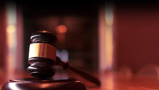 Wooden judge's gavel on a desk with blurred images of law books in the background