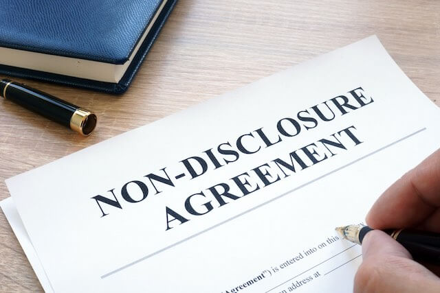 Close up of a person's hand signing a form labeled 'non-disclosure agreement'