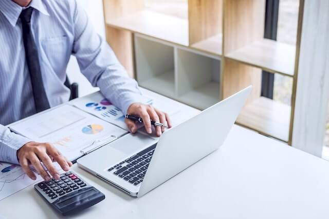 Businessman sitting at a desk with documents, a laptop and a calculator as he performs financial calculations