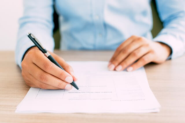 Close up of a person's hands filling out a questionnaire while she sits at a desk