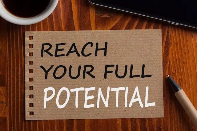 Words 'reach your full potential' written on a piece of cardboard sitting on a desk next to a pencil and a cup of coffee