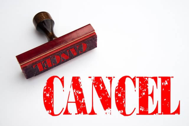Word 'cancel' in large red letters stamped on a white background with the rubber stamp lying next to it