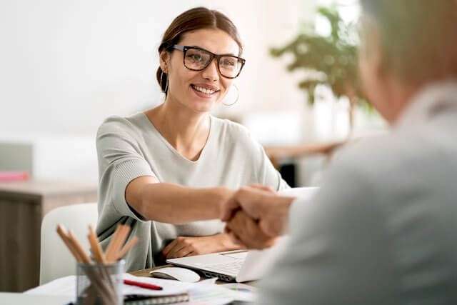 Focus on a smiling young businesswoman across a desk as she shakes the hand of a businessman during an interview