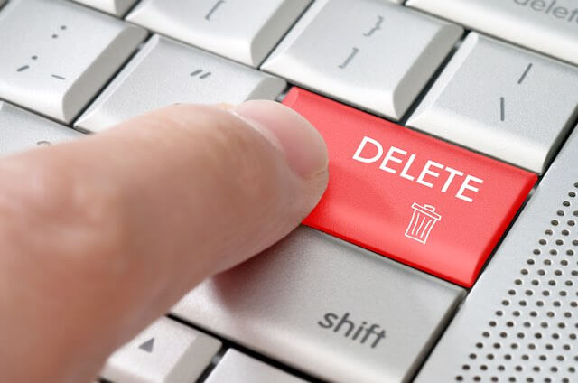 Close up of a person's finger pressing the delete key highlighted in a light red color on a keyboard