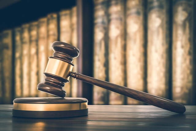 Judge's gavel sitting on a desk with a row of law books pictured in the background