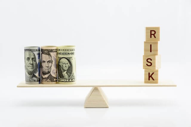 cash on one end of a seesaw scale with the word 'risk' in vertical block letters on the other end