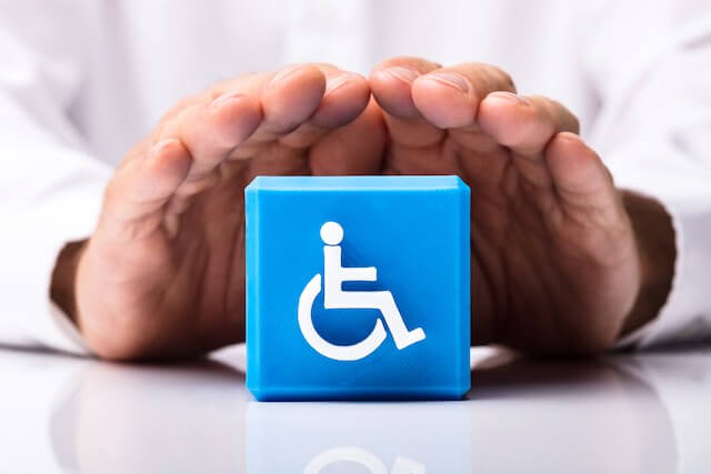 Close up of a person's hands shielding/protecting a blue block with the universal disability/handicapped icon on it