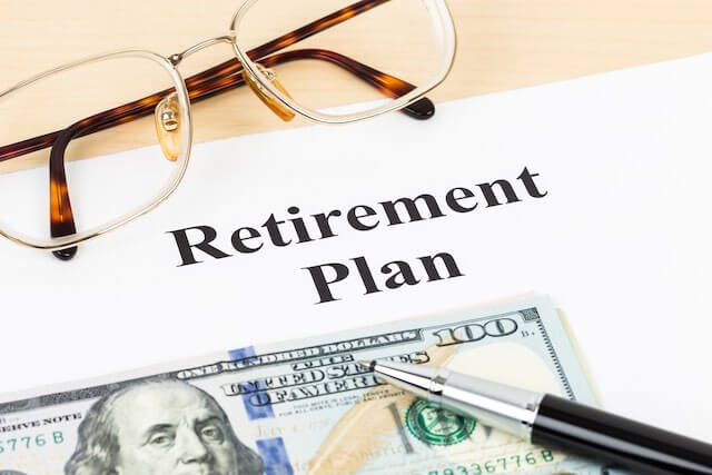 document on a desk labeled 'retirement plan' next to a $100 bill, pen and reading glasses