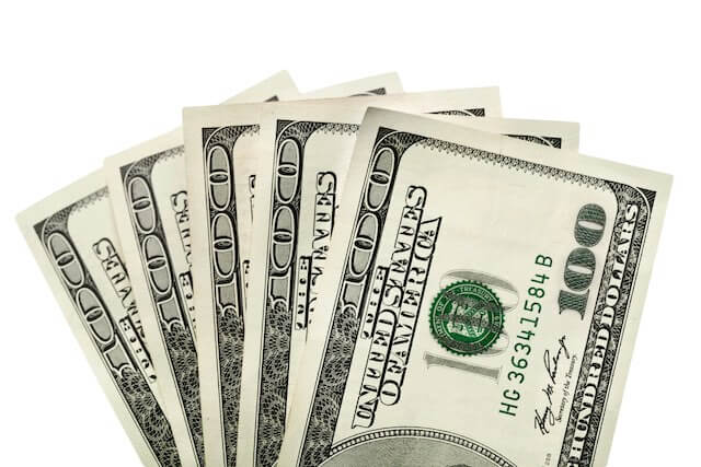 five $100 bills spread in a fan shape against a solid white background