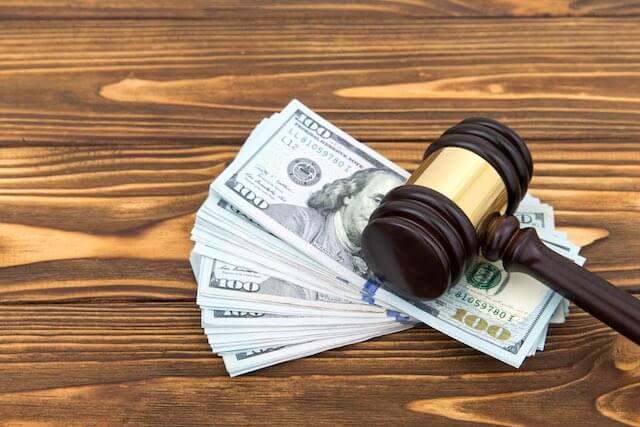 Spread of $100 bills underneath a judge's gavel lying on a wooden surface