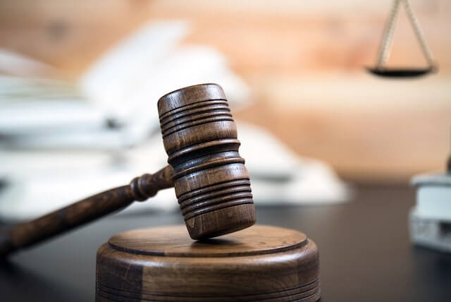 Wooden judge's gavel on a desk with a blurred image of law books and a justice scale in the background