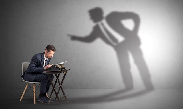 Male employee working hard on a typewriter with the shadow of an angry boss lurking over him