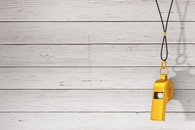 Golden colored coach's whistle hanging against a wooden background