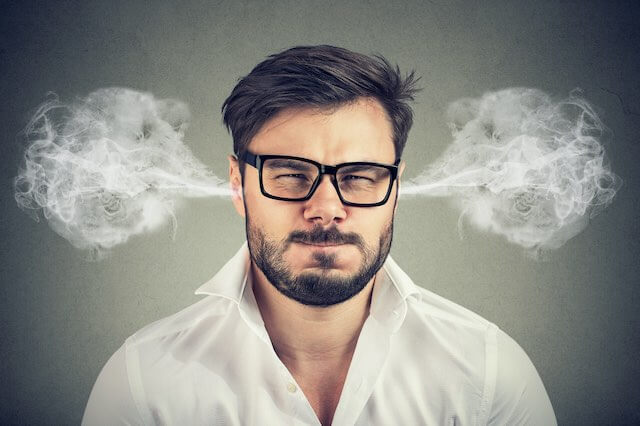 Younger adult man with his eyes closed and a tense expression of anger on his face with smoke blowing out of his ears