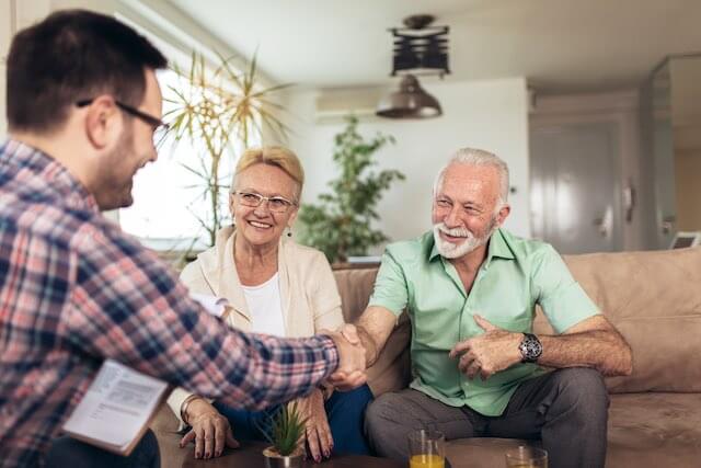 Young financial advisor meeting with a senior couple; the advisor is shaking hands with the man; financial planner, financial advisor, retirement plan