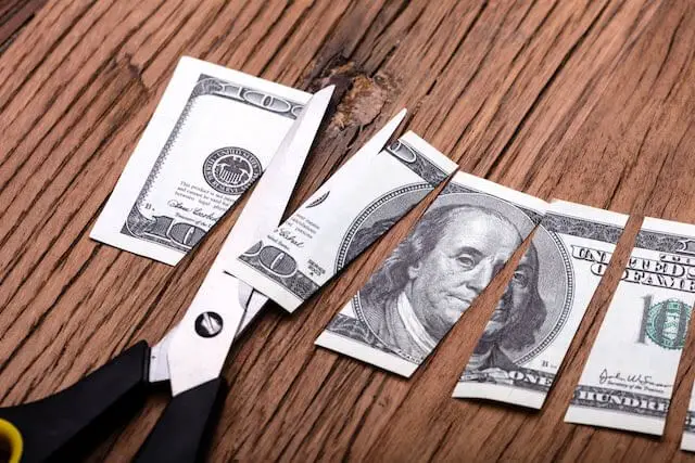 Scissors cutting a $100 bill into several pieces - pay cut, salary reduction, pay freeze