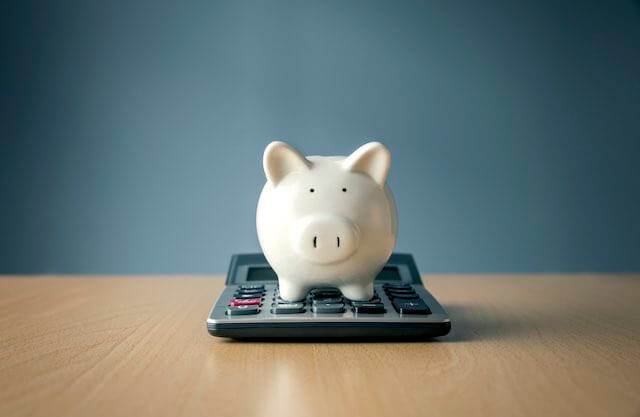Piggy bank sitting on top of a calculator depicting retirement savings, calculations, COLA