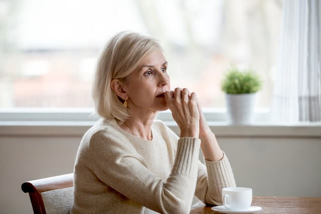 Senior aged woman sitting at the kitchen table deep in thought with a cup of tea in front of her