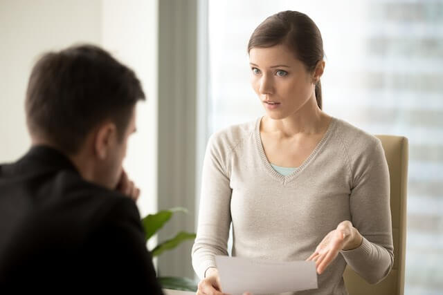 Female supervisor sits across the desk from an employee holding a sheet of paper as she talks to him during a discipline/counseling session