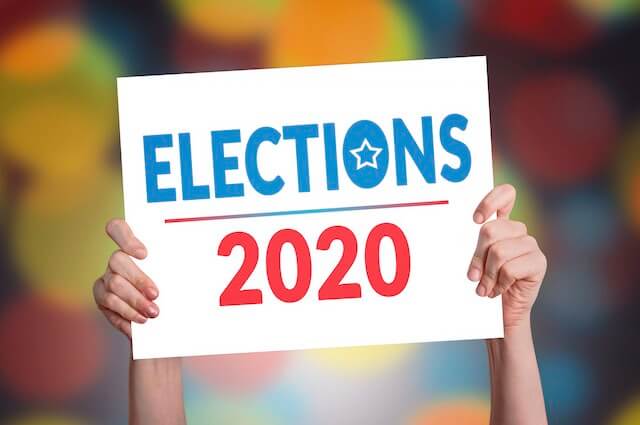 Close up of a person's hands holding a sign overhead that reads 'elections 2020'