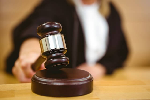 Close up of a gavel being held and tapped on its platform by a judge whose image is blurred in the background