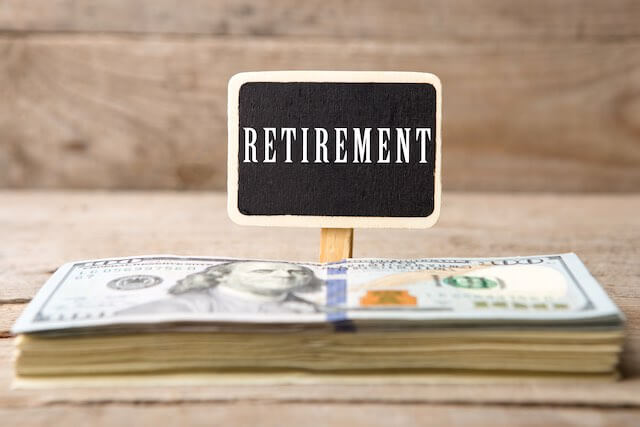 Stack of cash in front of a small black sign with white writing that reads 'retirement' against a wooden background