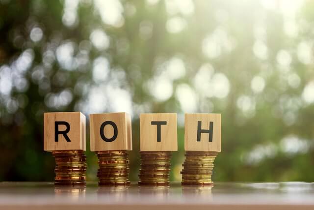 Wooden block letters sitting on the top of stacks of coins spelling the word 'Roth'