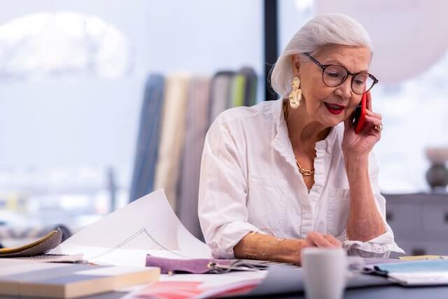 Senior aged businesswoman sitting at her desk talking on the phone while she looks at paperwork