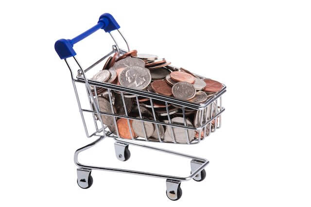 Shopping cart filled with coins against a solid white background depicting cost of living/inflation/COLAs