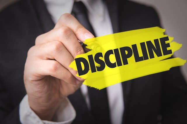 Businessman writing the word 'discipline' in black letters against a yellow background