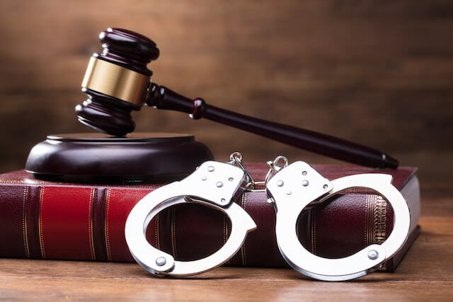 Wooden judge's gavel sitting on a desk on top of a law book and with a pair of handcuffs