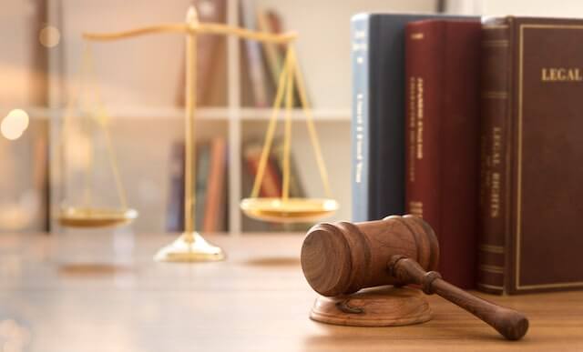 Wooden judge's gavel on a desk next to two law books and a justice scale seen in the background