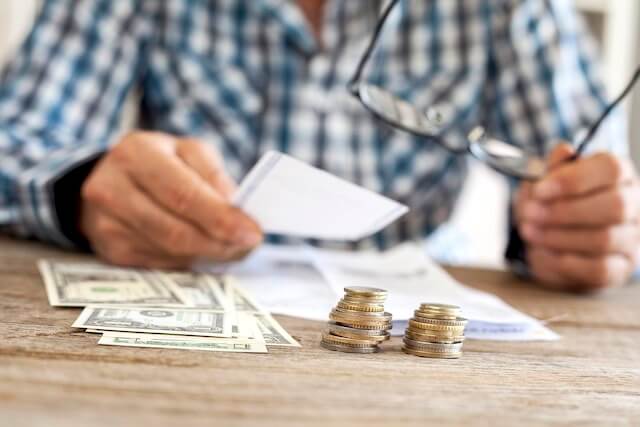 Close up of a man's hands sitting behind a desk studying bills with spread of cash and small stacks of coins in the foreground