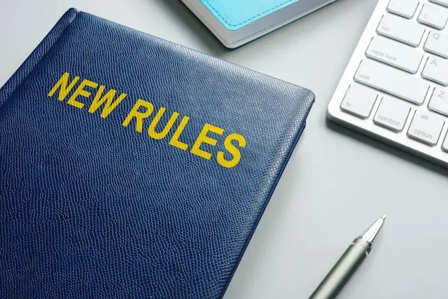 Book labeled 'new rules' sitting on a desk surface next to a pen and keyboard