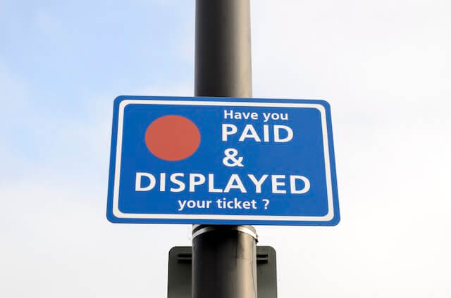 Paid parking reminder sign seen on a street light pole in a paid parking lot that reads 'have you paid and displayed your ticket?'