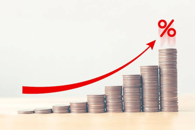Vertical stacks of coins growing in height from left to right with a rising red arrow over the top of them depicting positive investment gains/returns