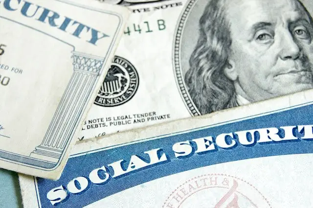 Close up of two Social Security cards lying on a surface next to a $100 bill