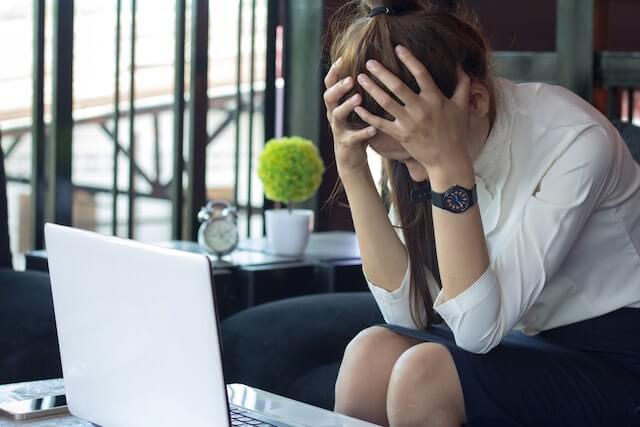 Businesswoman with her head in her hands sitting in front of her laptop appearing stressed out