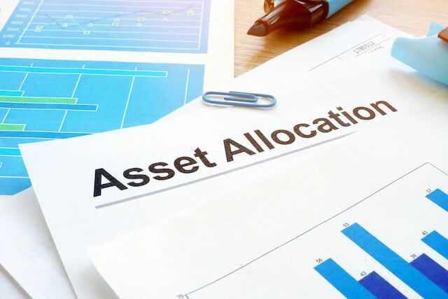 Words 'asset allocation' written on the top of a sheet of paper on a desk containing bar graphs