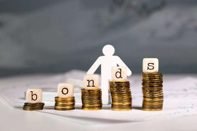 Stacks of coins growing in size from left to right with wooden block letters on top of each stack that collectively spell the word 'bonds'