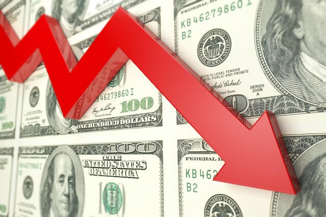 Red arrow trending downward imposed over a sheet of $100 bills depicting financial losses